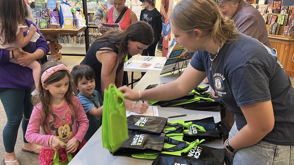 Parents sign their children in  at a preschool literacy event at a library. Children checking in receive a goodie bag.