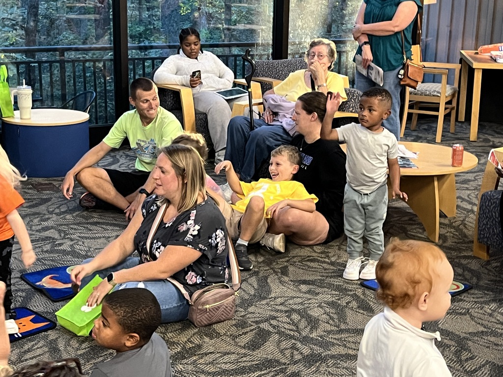 Children play play during a preschool literacy event at a library. Adults watch. 