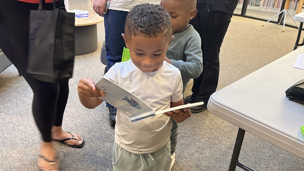 A small child holds up a copy of the book, The Rainbow Fish.