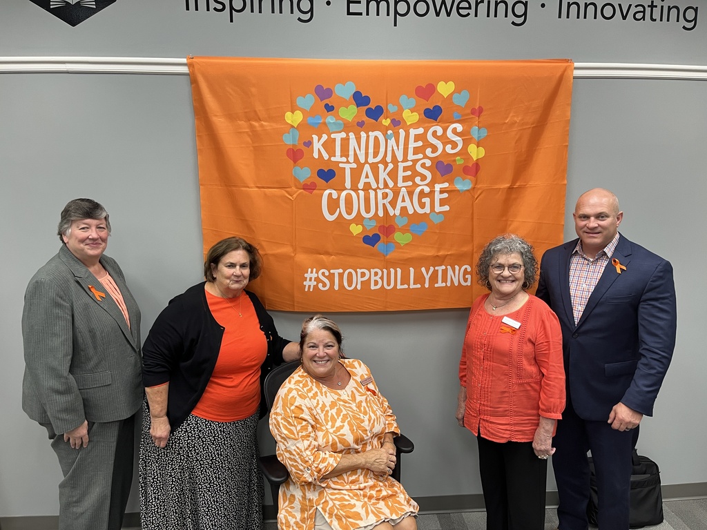 Four women and one man pose for a group photo in front of a banner on a wall that reads: Kindness takes courage. #stopbullying