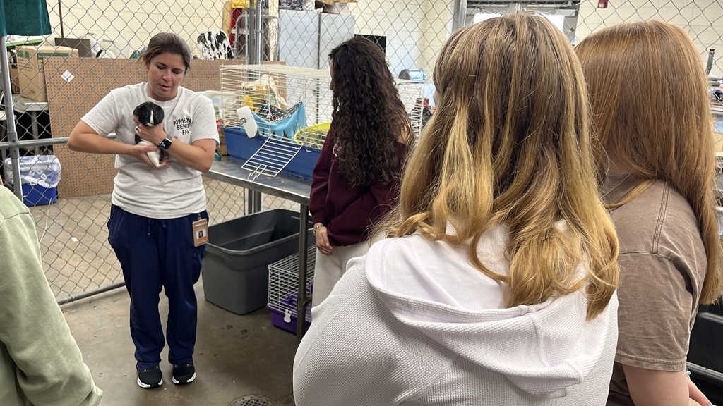 A teacher holding a guinea pig talks to her small animal care class about how to properly care for him.