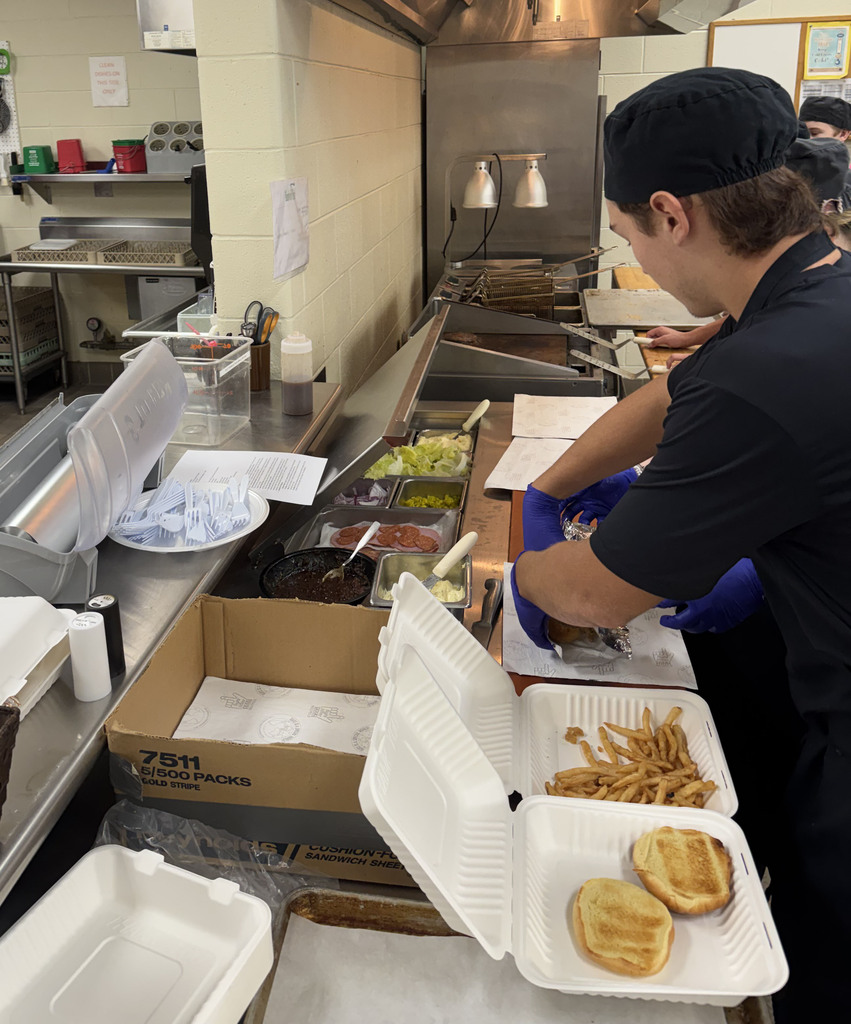 A culinary student plates hamburgers in styrofoam containers.