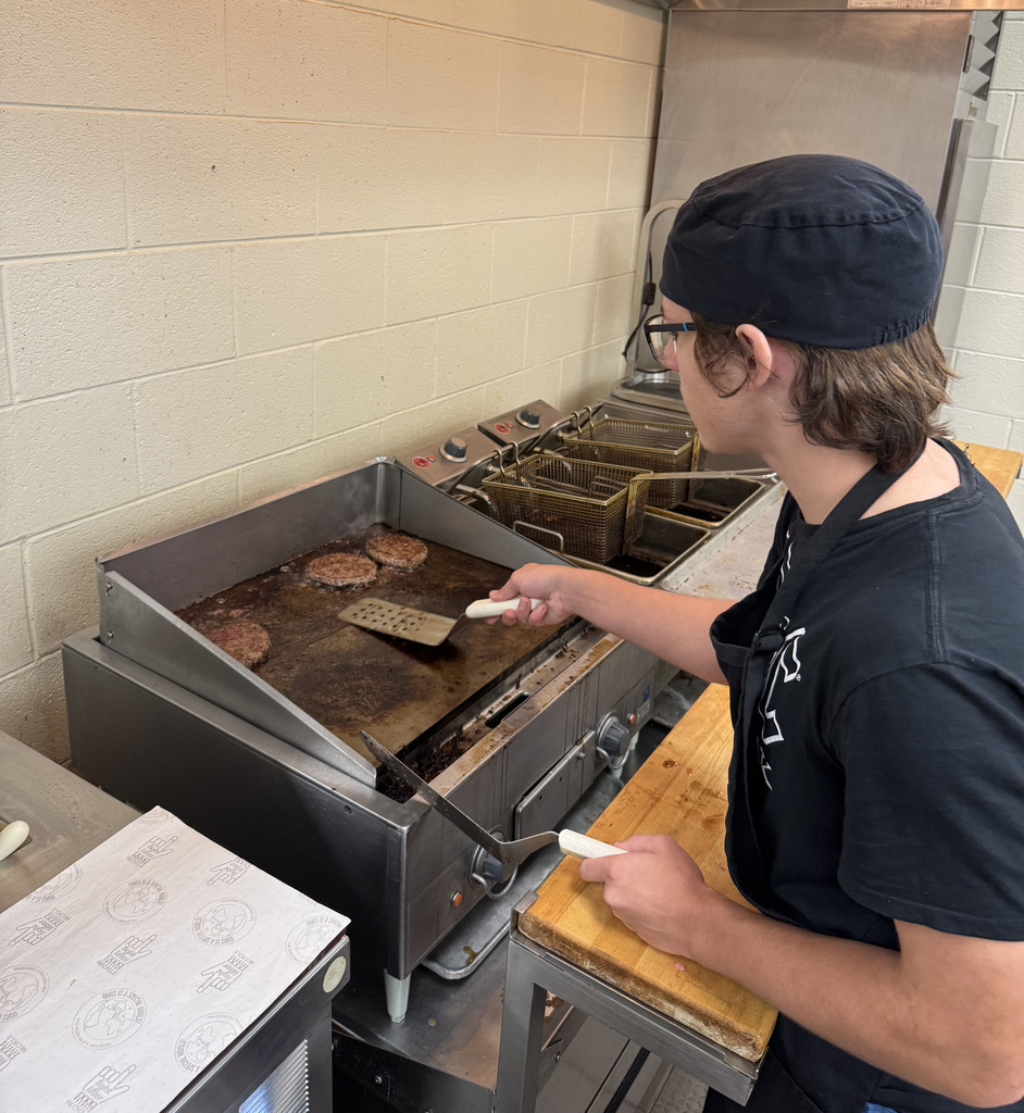A culinary student cooks hamburgers on a grill.