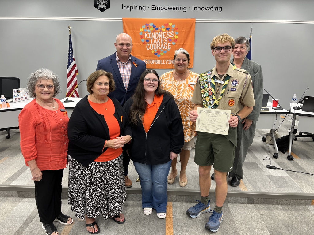 Five adults pose for a photo with two teens. One of the teens is wearing an Eagle Scout uniform and holding a certificate.