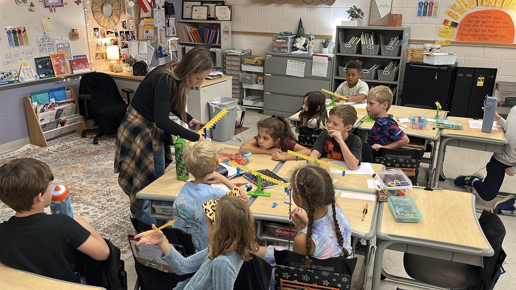 Students  listen to their teacher explain how a balance works as they explore equality and inequality.