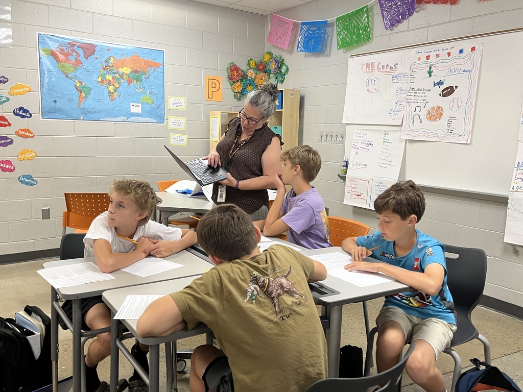 Students take an assessment in Spanish class to see what they know. A teacher helps a student.