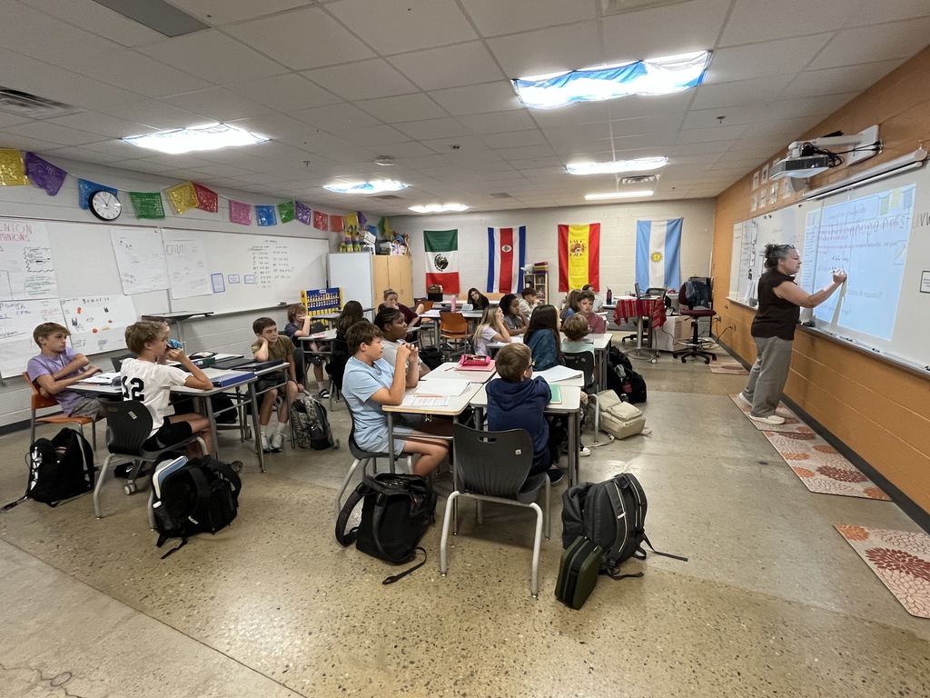 Students take an assessment in Spanish class to see what they know. A teacher gives them instructions.