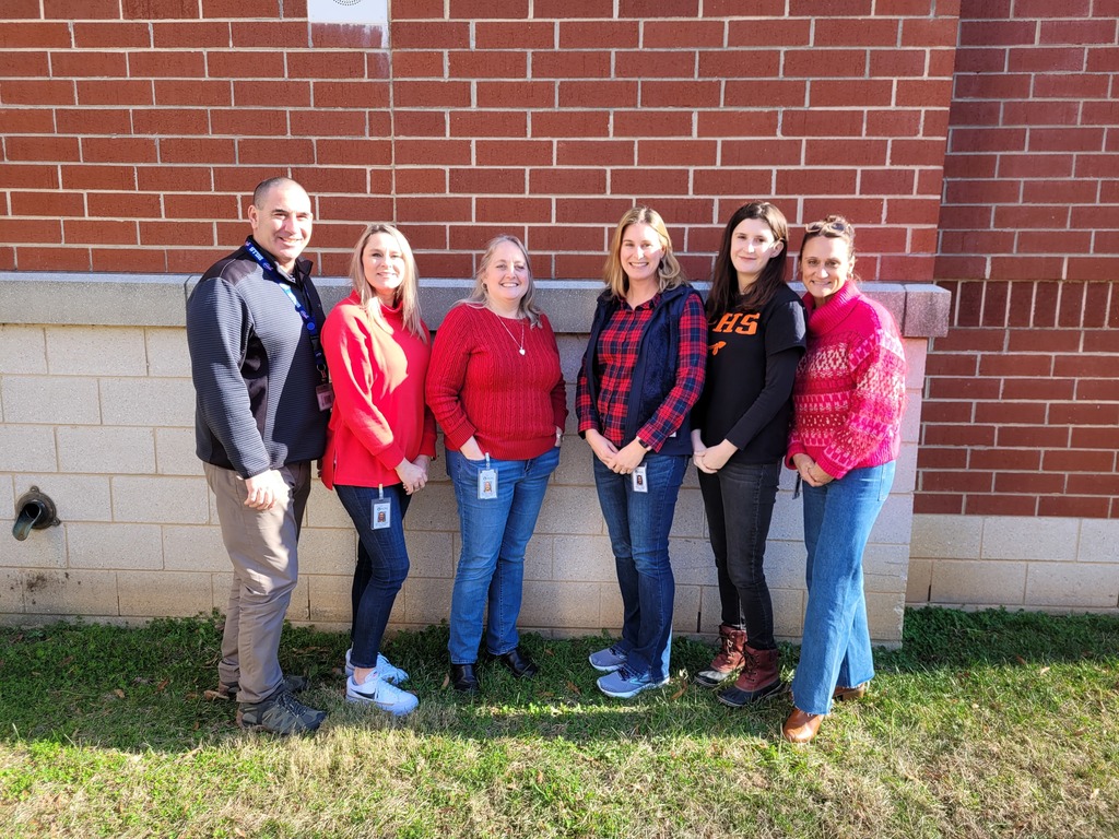 One man and five women smile at the camera while standing in front of a brick wall.