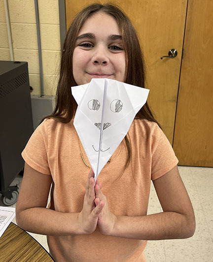 A student holds a paper airplane. 