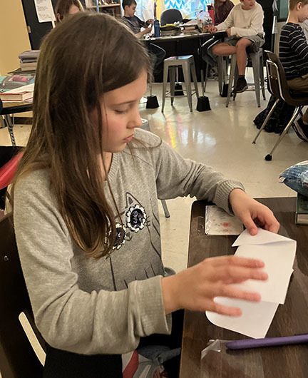 A student folds a paper airplane. 