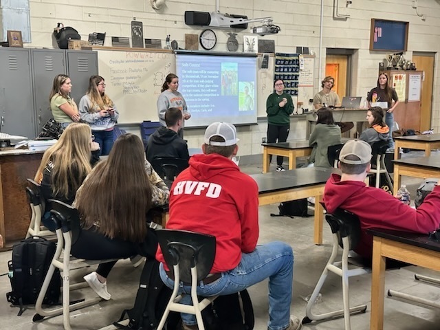 A group of students listen to a presentation by another group of students.