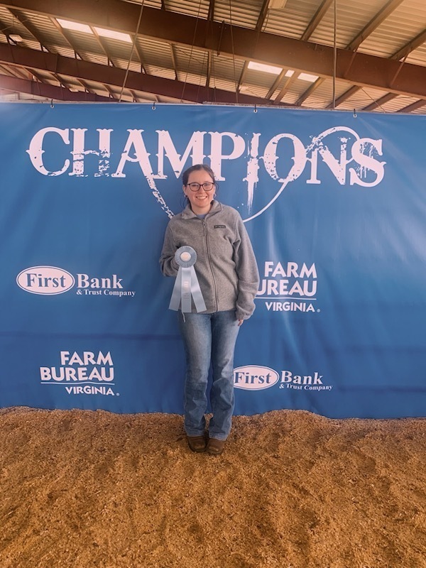 A girl holds a blue ribbon in front of a photo op backdrop.