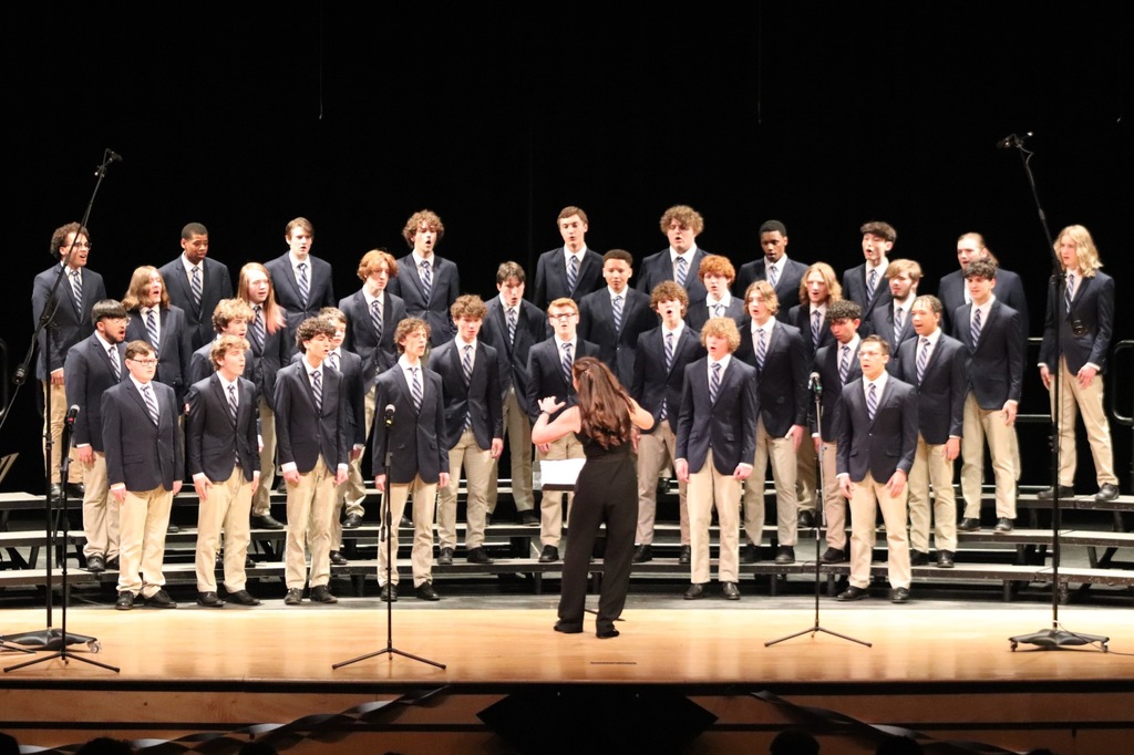 Onstage, a choir standing on risers and a woman conducting perform.