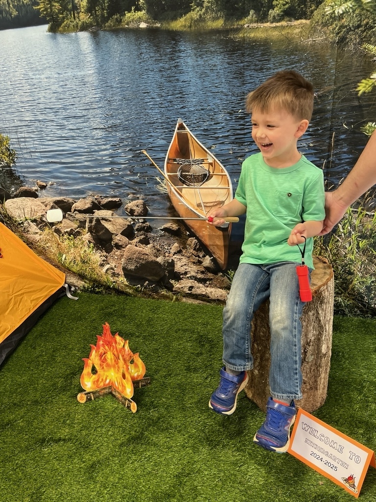 A child poses for a photo in front of a CAmping-themed backrop.