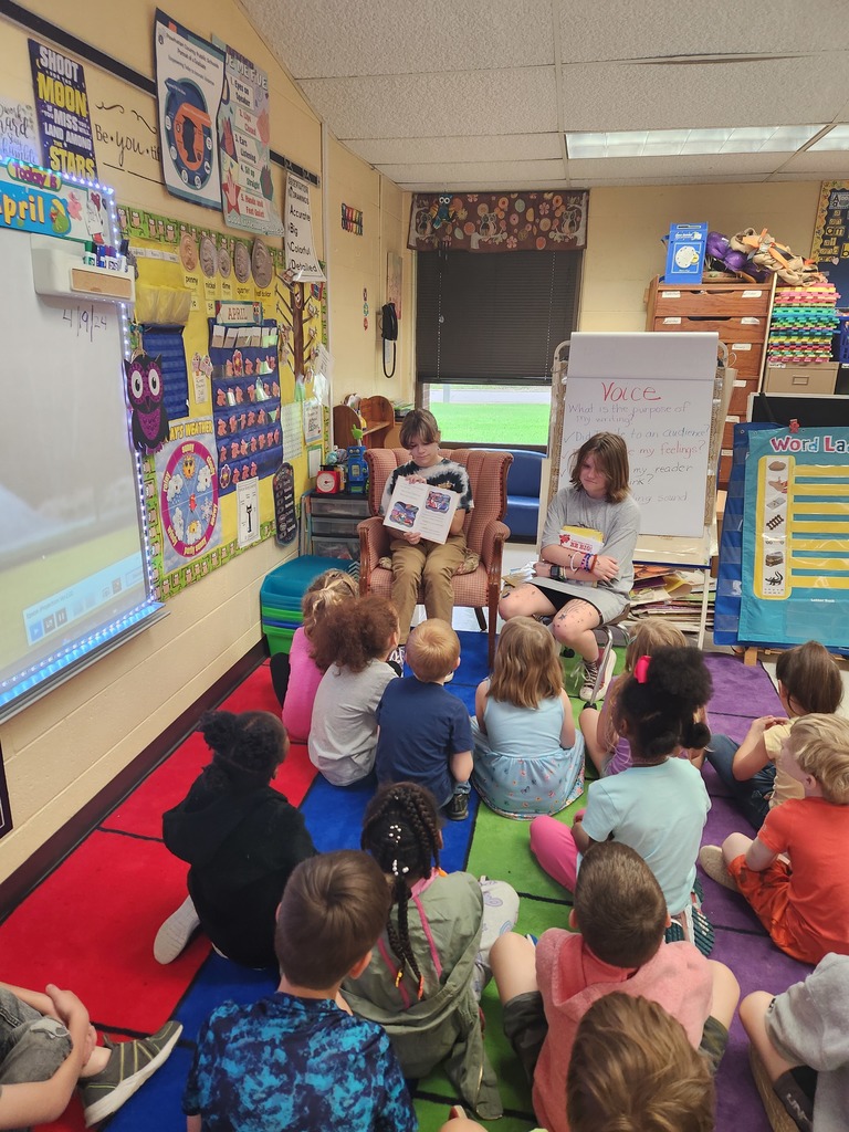 Elementary students listen to high schoolers read them a book.