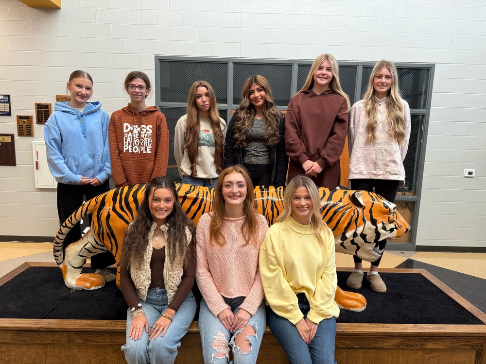 The colors day court members sitting in front of a tiger statue in the High School lobby
