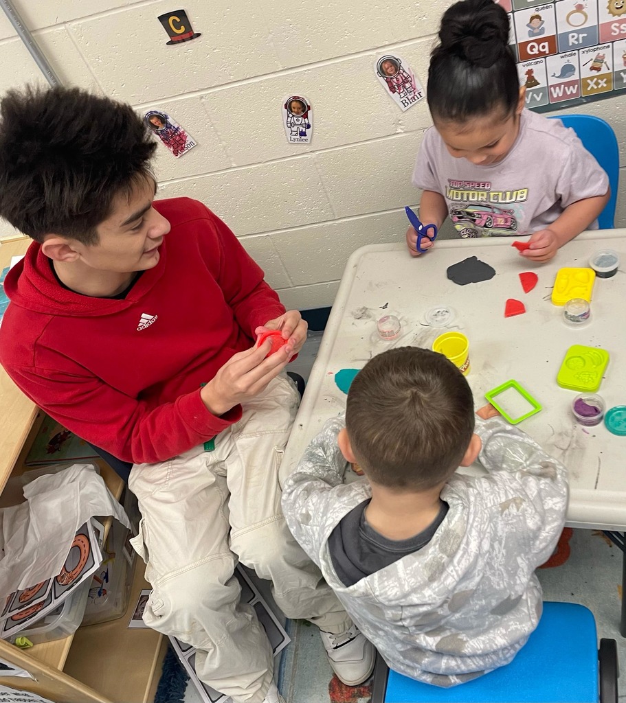 High school student playing with playdough with two preschool students