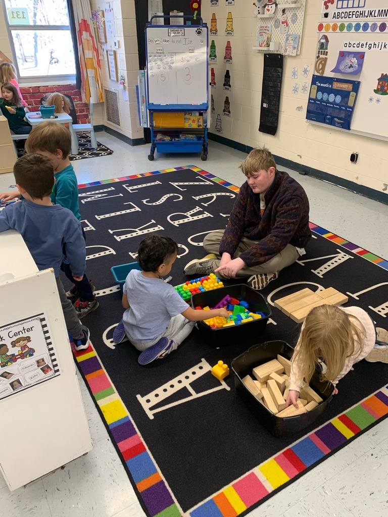 high school student sitting on a rug playing with colorful blocks with two preschool students