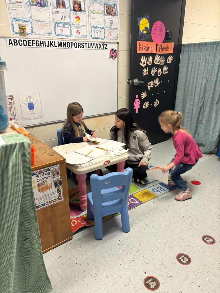 female preschool student showing a high school student her work in a notebook