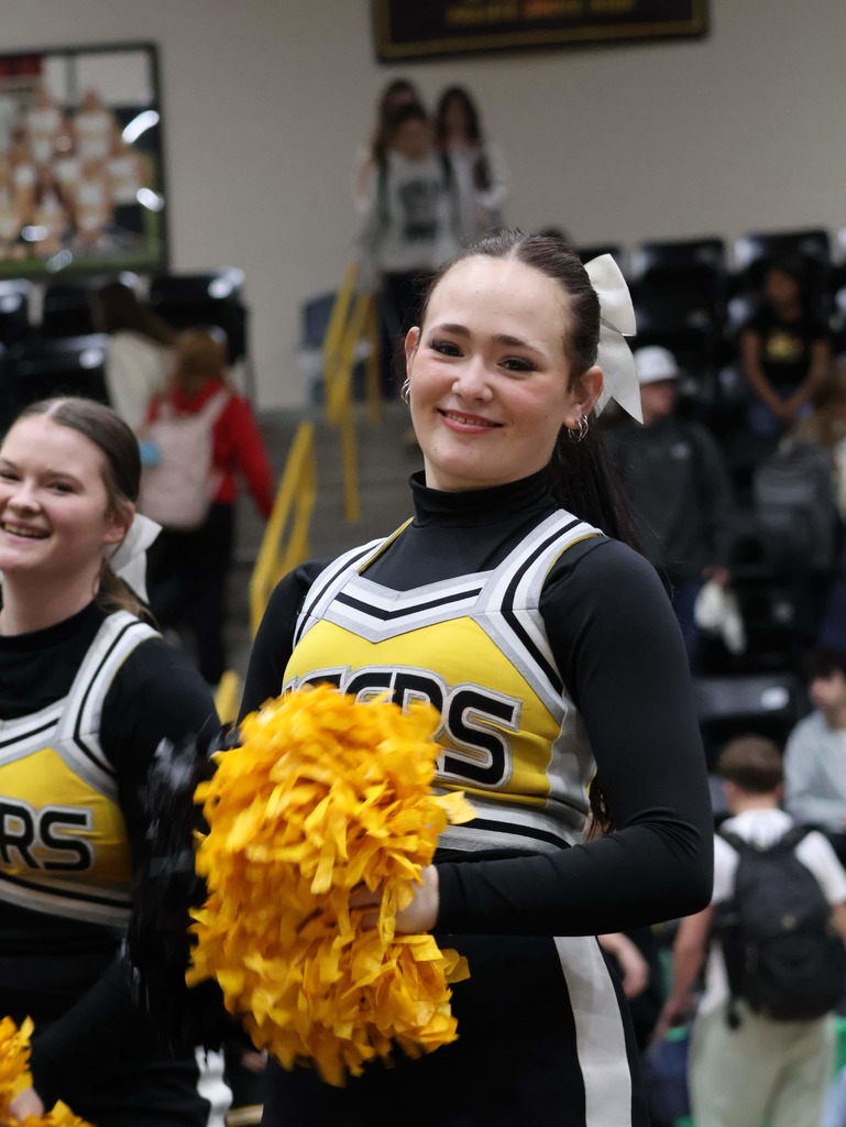 Junior High cheerleader in her uniform holding gold pom poms and smiling at the camera