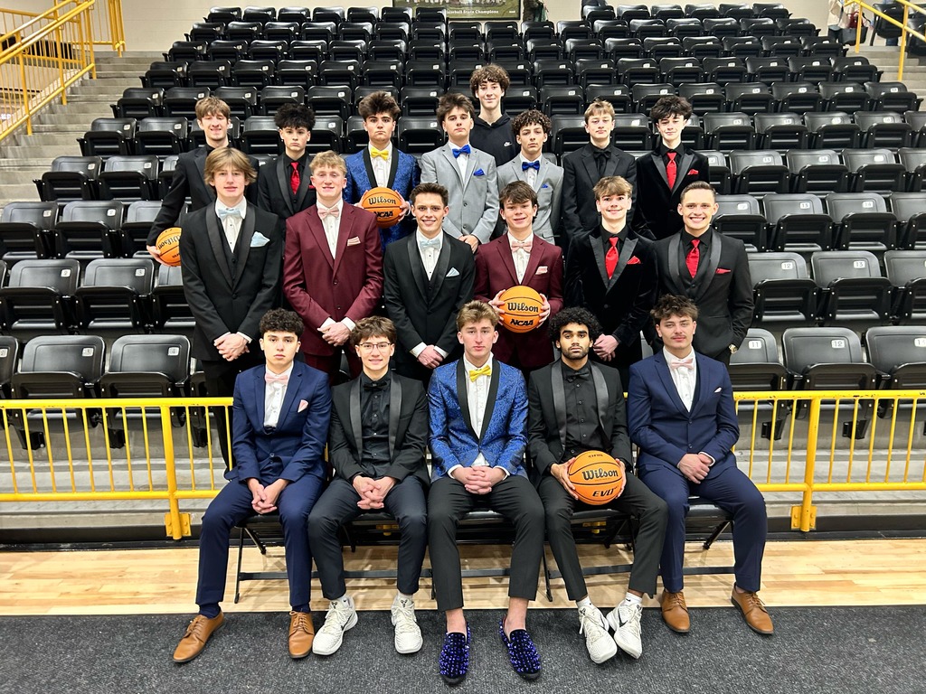The colors day court escorts, the boys basketball team, dressed in suits gathered together smiling at camera