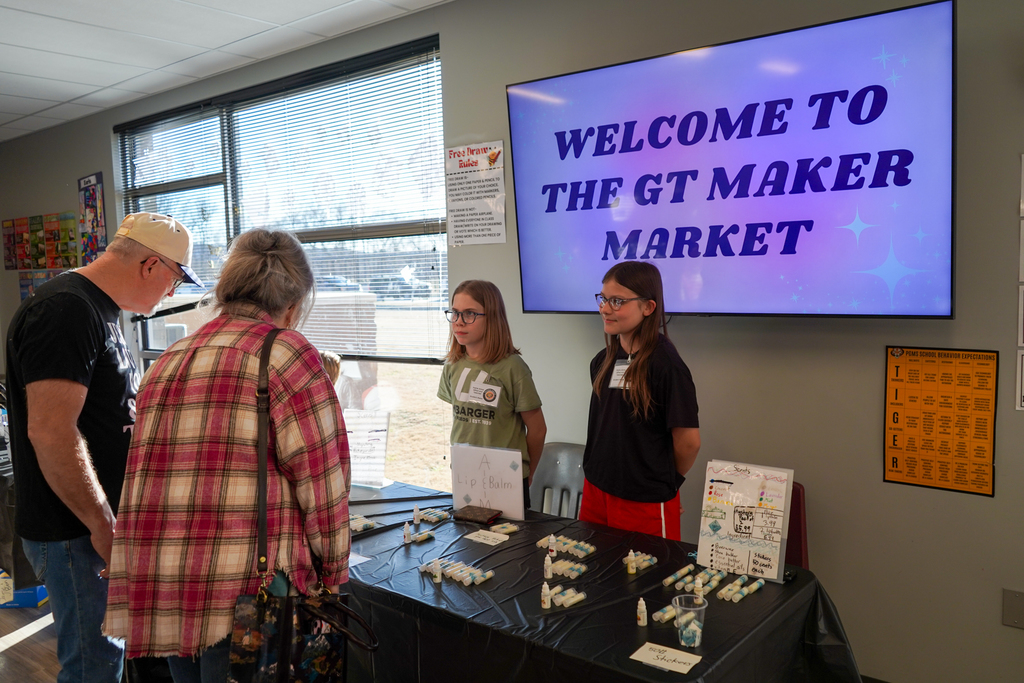two middle school girls standing behind their table display with a sign in the background that says welcome to the GT maker market