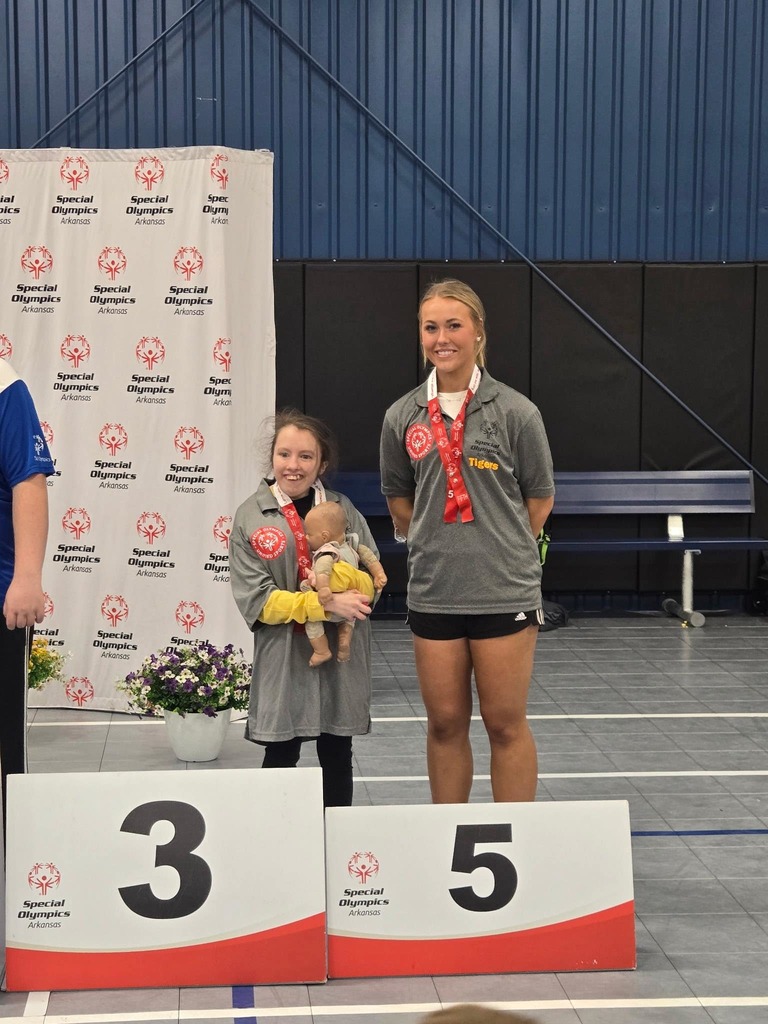 2 students standing together and smiling up at the special olympics award platform after receiving their medals