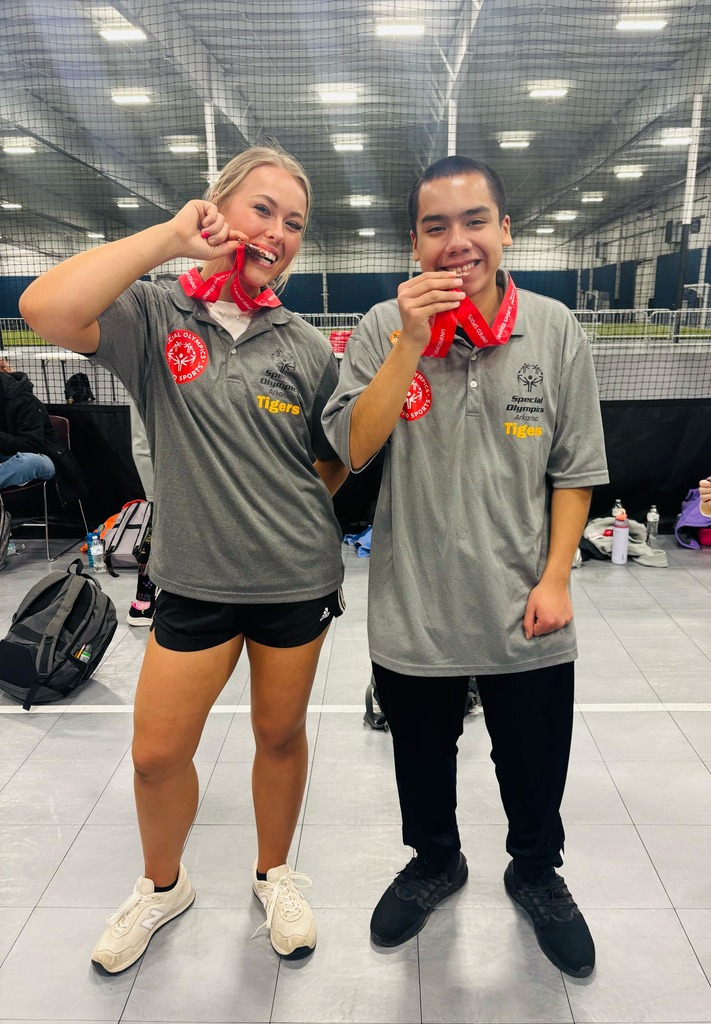 2 pg athletes standing together biting their placement medals