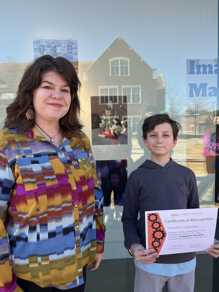 Art teacher Katie Terry with student Tucker smiling with his certificate of recognition for a robot art display