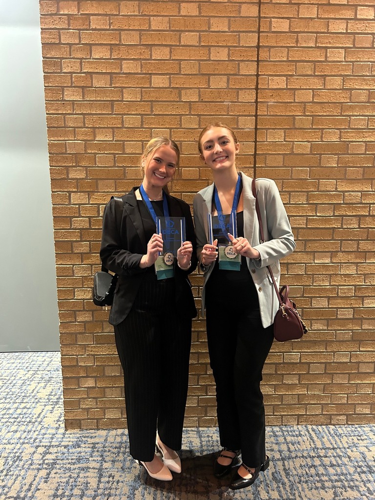 two high school girls smiling with their DECA medals and plaques