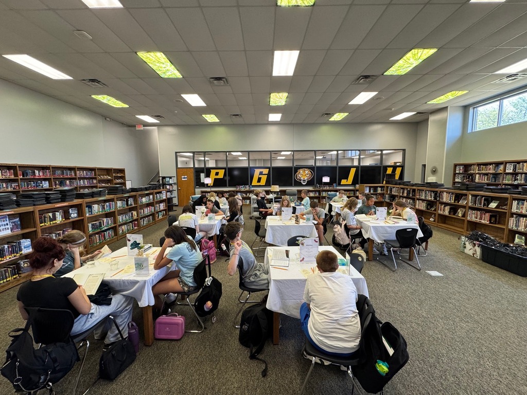 Students browse books at eight library tables.