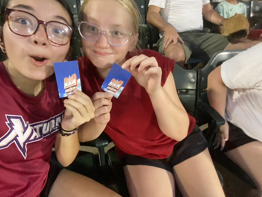 Two students seated at the Naturals game hold up gift cards