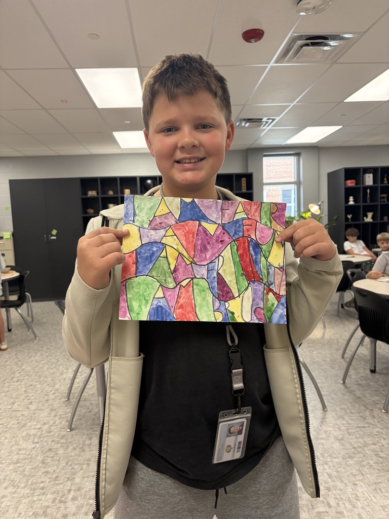 A student smiles while he shows his art work