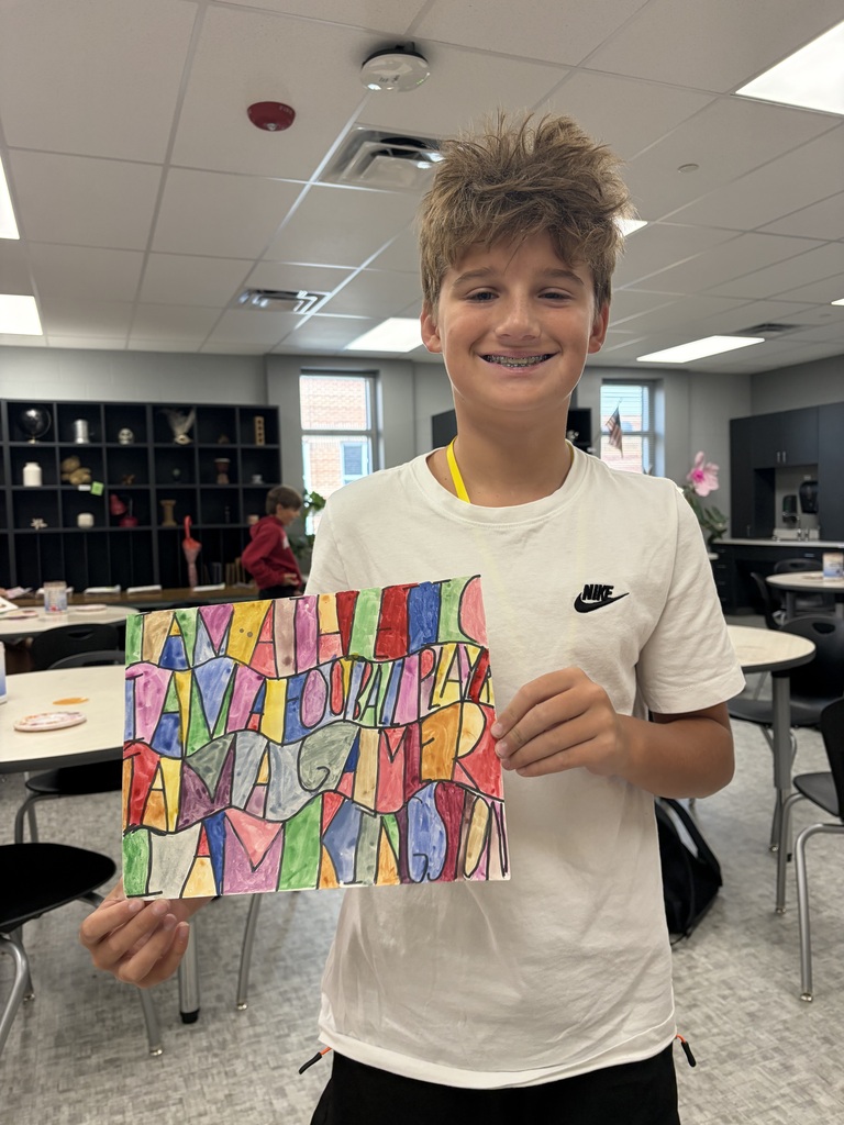 A student holds his word art for a photo in the art classroom.