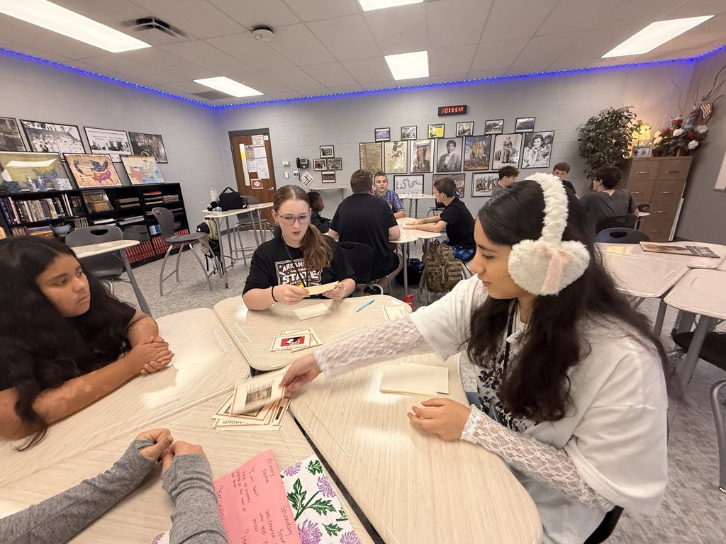Four students are seated at a table. One draws a card for a game of slapjack