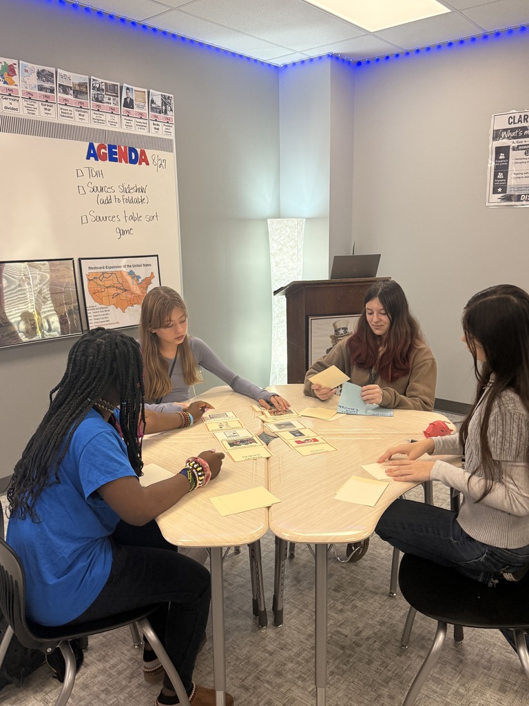 Four students sit at a table playing slap jack as they identify primary and secondary sources.