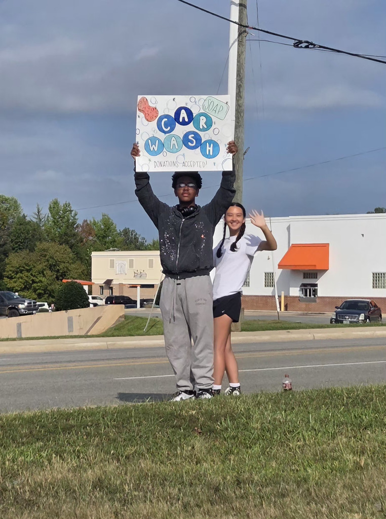 students holding carwash sign next to road