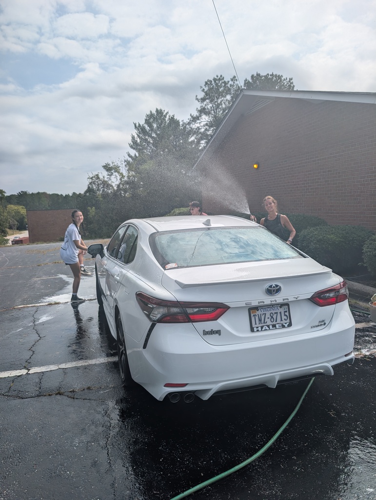 people washing a white car and the female on the right spraying water