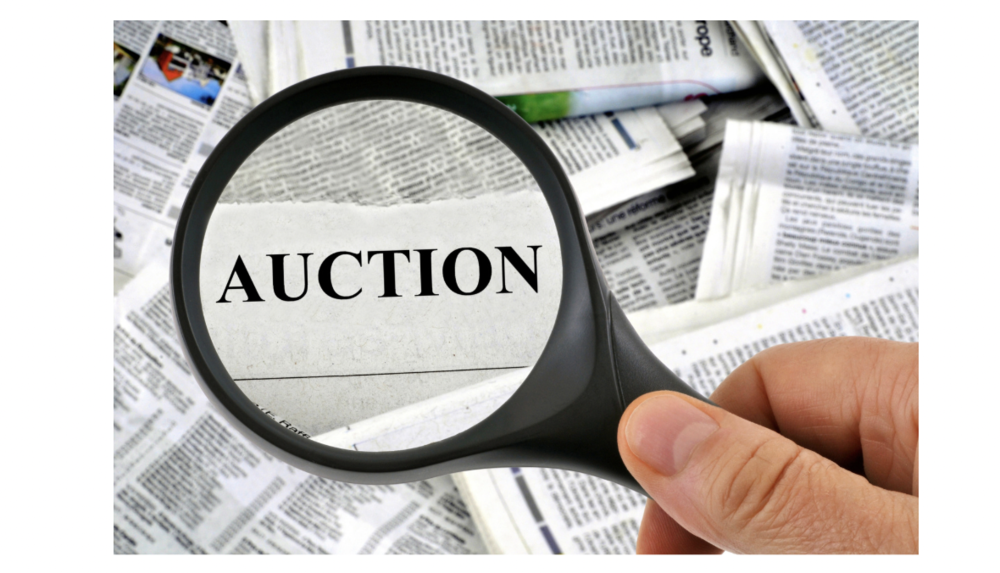 A magnifying glass highlighting the word AUCTION printed on a newspaper.