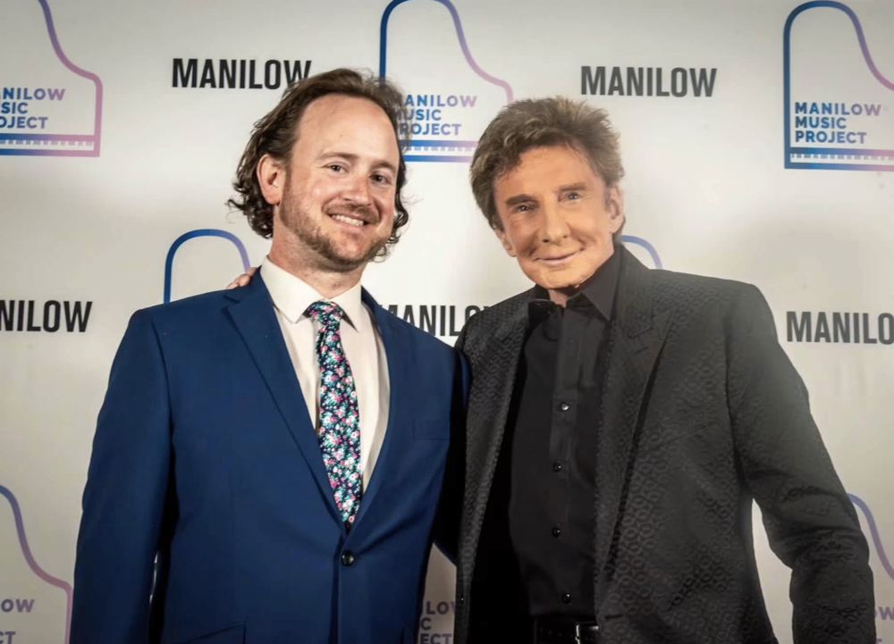 Kyle Phillips and Barry Manilow in front of the Mainlow Music Project's Step and Repeat