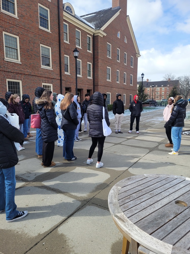 Princeton High school students bundled in winter coats gather in a courtyard outside a classic red-brick Miami University building on a cold, partly cloudy day during their campus tour.