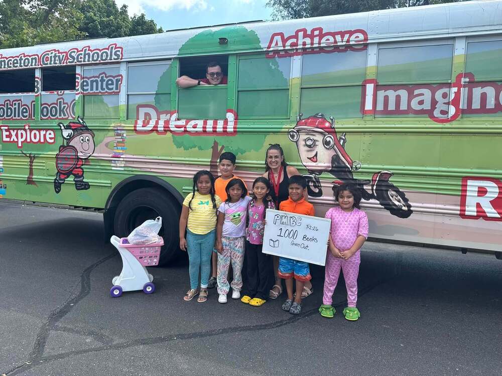 Five kids with Princeton librarian Stephanie Behr in front of the Princeton Mobile Book Center with Ms. Behr's son  smiling through the window.