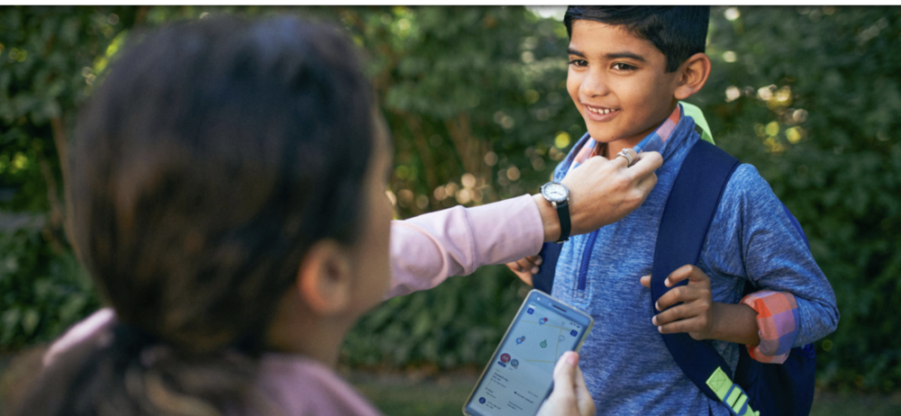 Parent holding app to track bus while helping child with backpack get ready