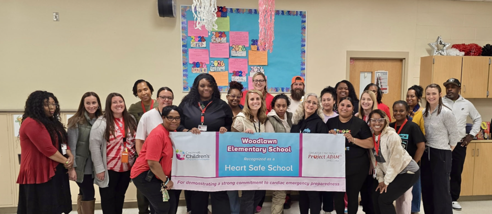 Woodlawn Elementary Staff behind a banner that reads "Woodlawn Elementary is a Heart Safe School"
