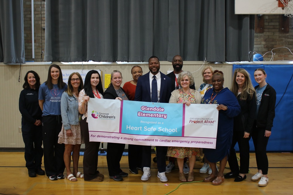 Representatives from Glendale Elementary, Cincinnati Children's Heart Institute, and Project ADAM posing for a picture while holding up a banner that recognizes Glendale Elementary as a Heart Safe School