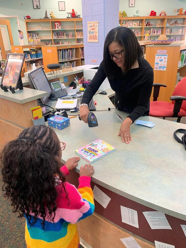 adult checking out a book in the library with a student