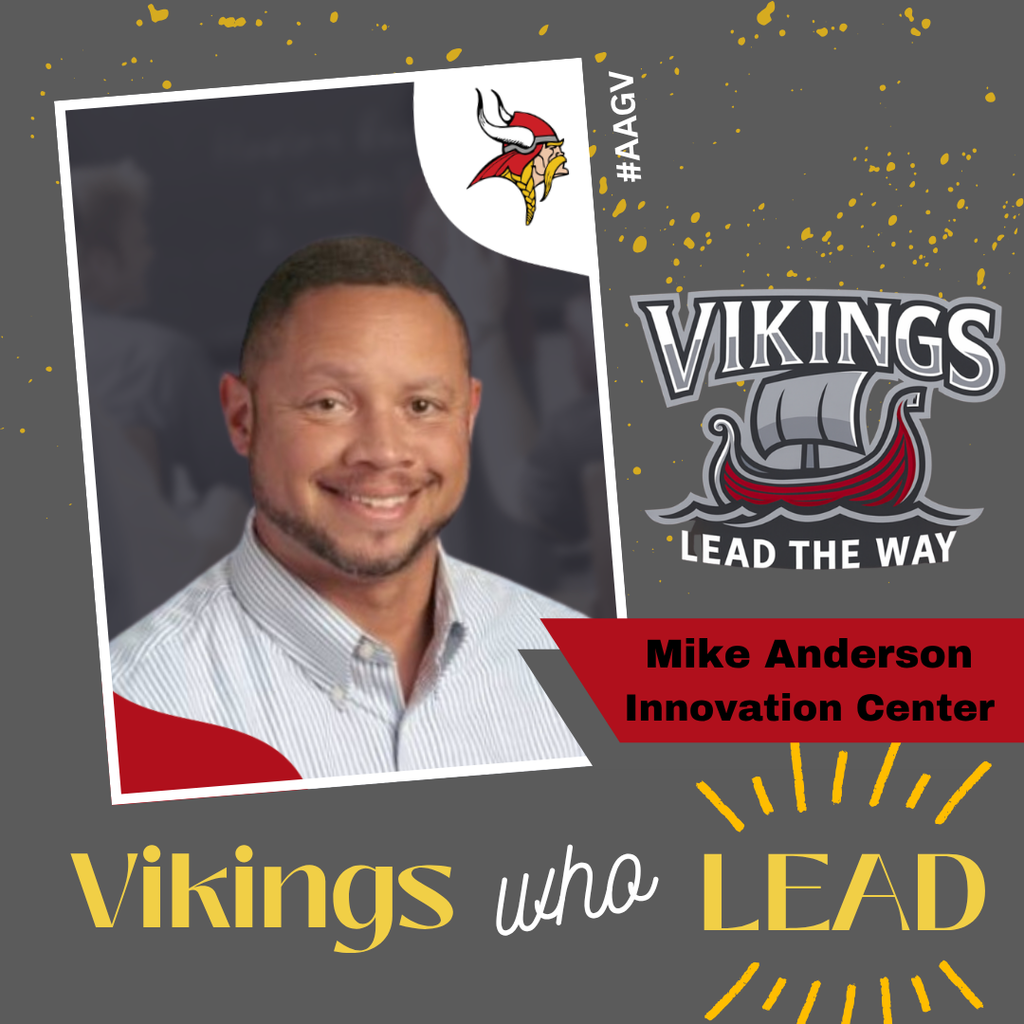 "Professional headshot photograph of Mike Anderson from Innovation Center wearing a light blue striped button-down shirt, smiling at the camera against a dark background. A small Viking mascot logo with red and yellow colors appears in the upper left corner of the tilted white photo frame. The image is set against a gray background decorated with gold confetti. The Vikings logo featuring a viking ship with 'Lead The Way' motto appears in the top right. Text at bottom reads 'Vikings who LEAD' with 'Vikings' and 'LEAD' in gold and 'who' in white script. A red banner identifies 'Mike Anderson, Innovation Center.' Hashtag #AAGY appears vertically along the right edge."