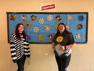 two people standing in front of a bulletin board
