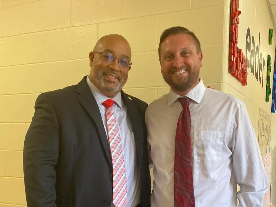 two people wearing ties and long sleeve shirts in front of a wall