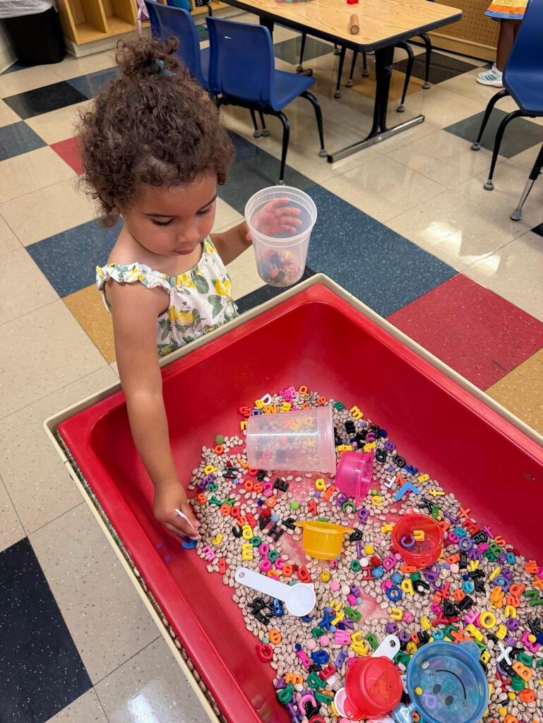 student exploring the sensory table filled with beans and plastic letters